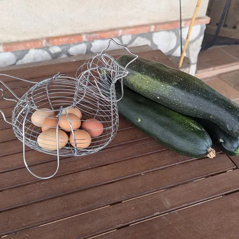Huevos en una cesta de alambre con forma de gallina y calabacines del huerto