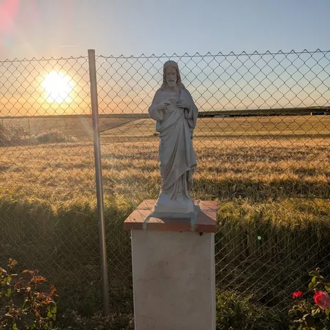 Imagen del Sagrado Corazón sobre un pedestal, ante un campo de cereal con el sol bajo